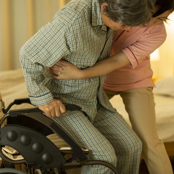 Une infirmière lève une personne en situation de handicap moteur pour la poser dans son lit