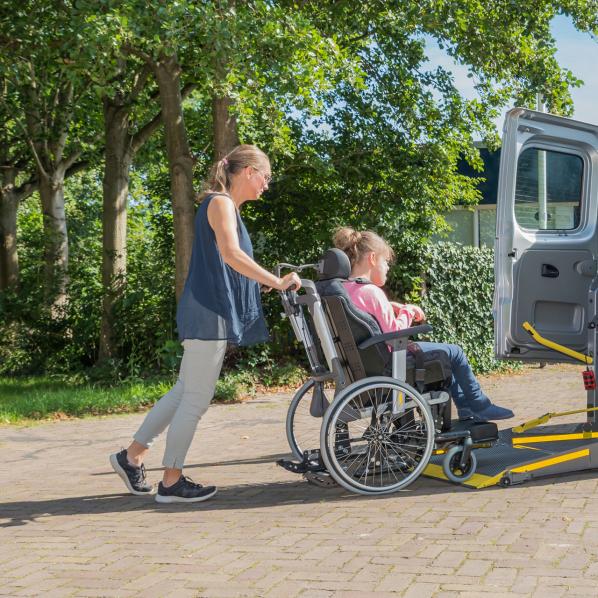 Une personne pousse le fauteuil roulant de l'enfant dans la voiture pour qu'elle puisse être transporter à l'école