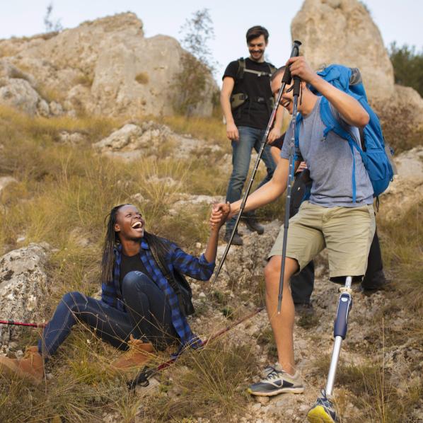Trois jeunes font une randonnée. Le jeune homme ayant une prothèse de jambe aide une jeune femme à se relever du rocher