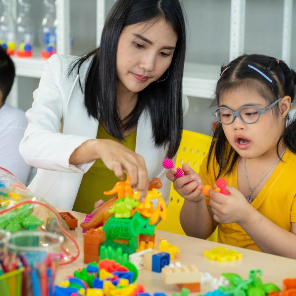 Une enfant autiste joue avec des jeux pour améliorer sa motricité dans une classe avec la maîtresse