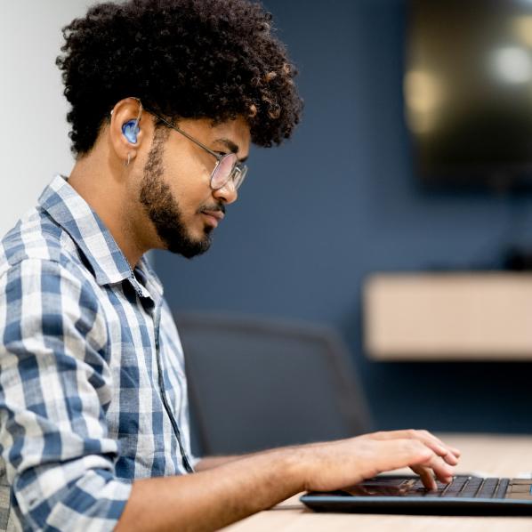 Un jeune homme qui possède des appareils auditifs est en train de travailler sur son ordinateur portable