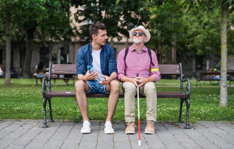 personne âgée non voyante assise sur un banc à côté d'un jeune homme avec qui elle discute
