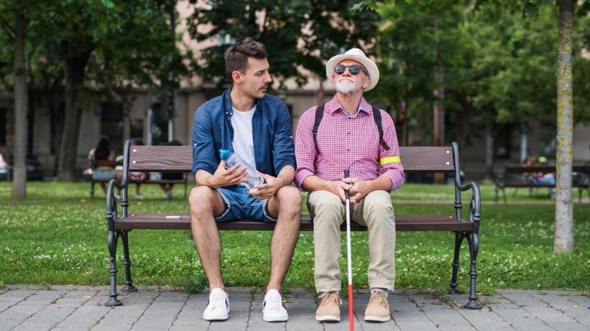 personne âgée non voyante assise sur un banc à côté d'un jeune homme avec qui elle discute