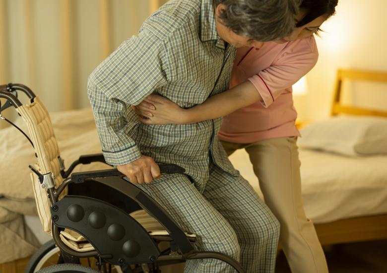 Une infirmière lève une personne en situation de handicap moteur pour la poser dans son lit