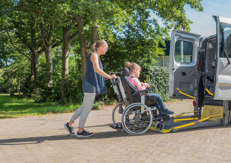 Une personne pousse le fauteuil roulant de l'enfant dans la voiture pour qu'elle puisse être transporter à l'école