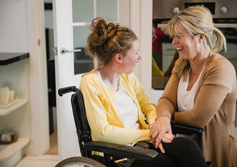 Maman et sa fille handicapée, en fauteuil roulant se prenant par la main et souriant