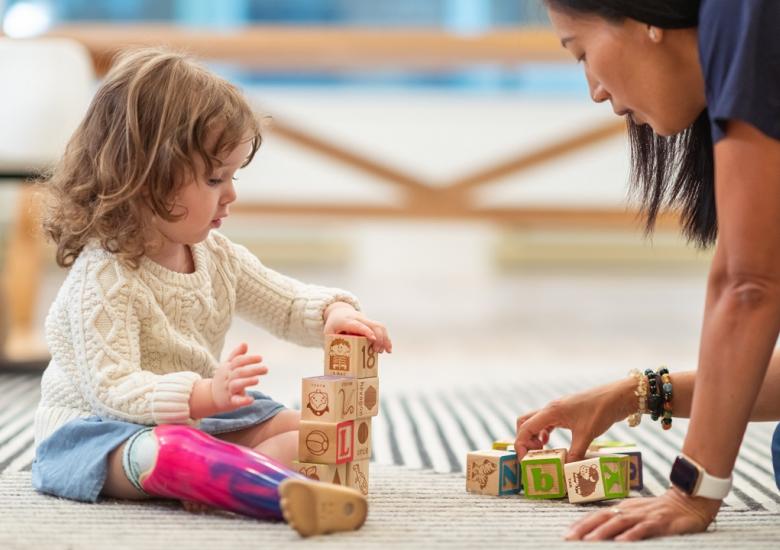 jeune femme aide à domicile jouant avec une petite fille handicapée